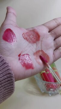 Applying pink lip tint on palm using brush applicator. Close up view. Lip color product swatch for cosmetic beauty presentation.