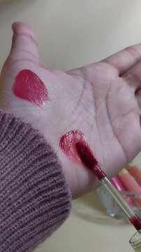 Applying red lip tint color on palm skin using brush applicator. Close up view. Lip product swatch for beauty cosmetic presentation.