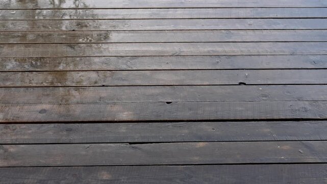 Wet wooden deck boards gradually drying after a rain shower, with the water evaporating from the dark, damp surface and revealing the natural texture of the weathered timber planks