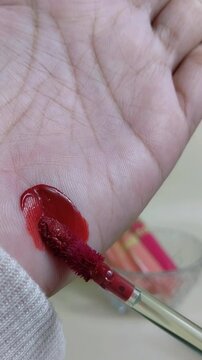 Applying dark red lip tint to hand skin using makeup brush. Vertical close up view. Deep bold lip color swatch for beauty presentation.