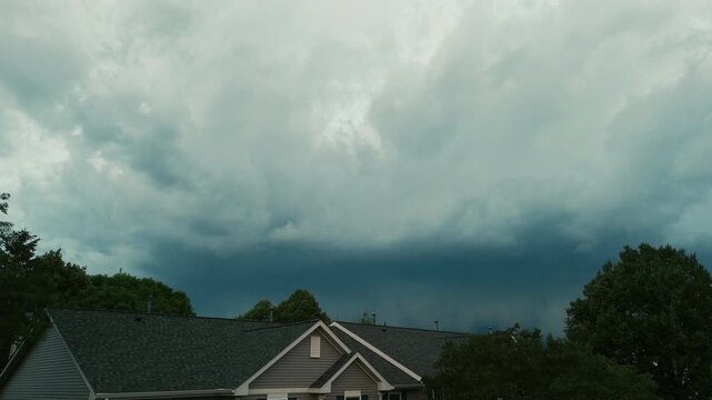 Massive storm clouds moving over a suburban neighborhood before severe weather. Dramatic shelf cloud forming above residential homes with dark skies, creating an intense and threatening atmosphere.