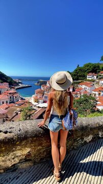 Tourist woman with straw hat looking at Cudillero coastal village in Asturias, tour tourism, travel in Spain
