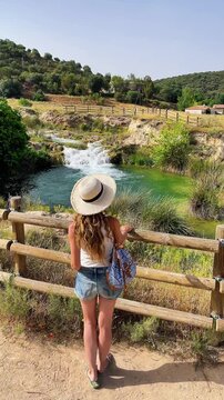 Woman with straw hat looking at Ruidera waterfall and green lagoon in Spain