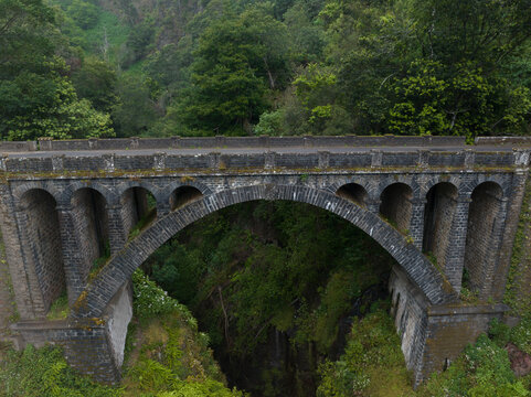 Aerial view of an old stone arch bridge spanning a deep, lush, forested ravine in Madeira.