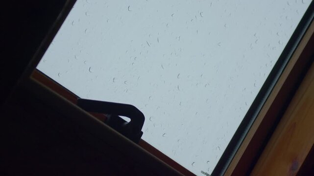 Skylight window rain glass, static tripod shot. Close view of water droplets streaming down glass surface of wooden attic roof window in rainy day.