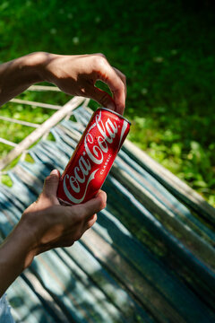 Minsk, Belarus - July 3, 2026: A cropped shot of a person holding a chilled can of Coca-Cola Classic over a fabric hammock in a sunlit backyard