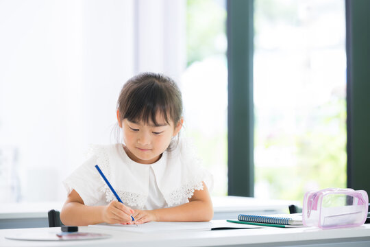 教室で勉強に集中して取り組む幼稚園・小学生位の女の子・塾や学校、受験や勉強、学習のイメージ	