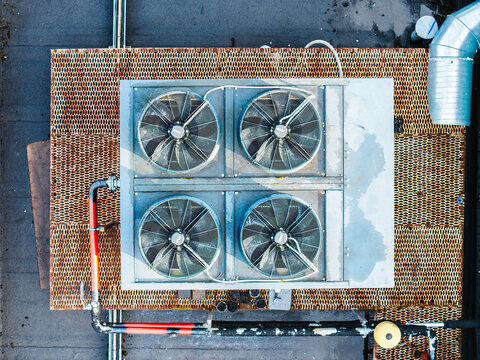 Aerial view of an industrial HVAC unit with four large fans mounted on a rusty metal grate rooftop in Riga, Latvia.