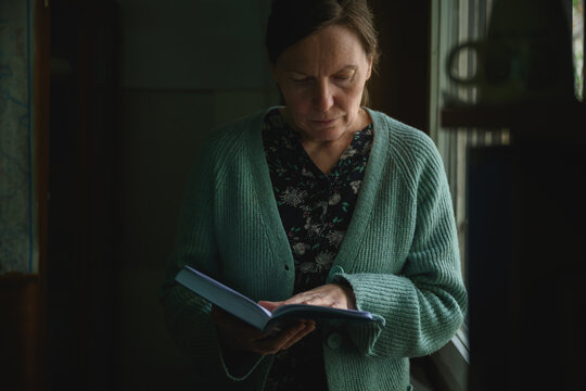Female standing in dim interior of an old office reading a book, quiet introspective moment in soft ambient light