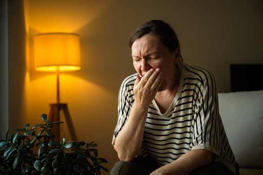 Tired woman yawning at home after a long day. Fatigue, work-life balance, evening routine and healthy rest concept.