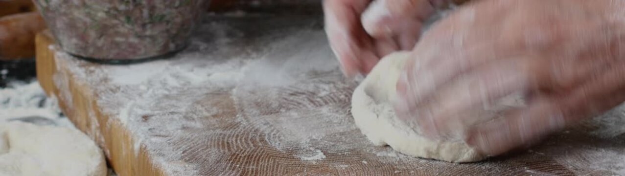 Hands preparing homemade dough on a floured wooden board making individual pieces for traditional food preparation.