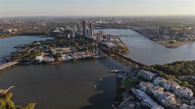 Aerial drone video panning left over Rhodes in Sydney, featuring a ferry on the Parramatta River, waterfront apartments, urban parkland, and modern residential development in Australia