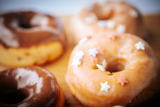 Assorted mini donuts with shiny chocolate and vanilla glaze, star decorations and soft focus on a wooden board