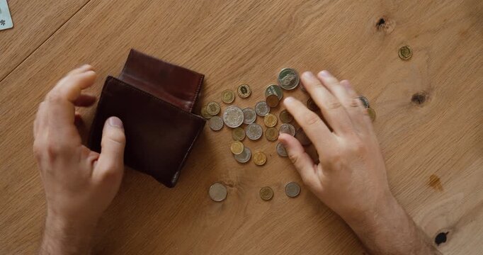 Top view of a person emptying coins from a wallet onto a wooden table. Financial concept of savings, budgeting, loose change, expenses, and personal finance.