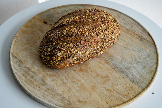 Artisan multigrain bread loaf with a golden seeded crust resting on a round wooden board, a wholesome homemade loaf full of grains against a soft background.