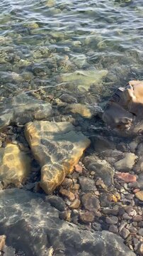 Clear water rippling over colorful rocks and pebbles on a sunny shoreline. Environment