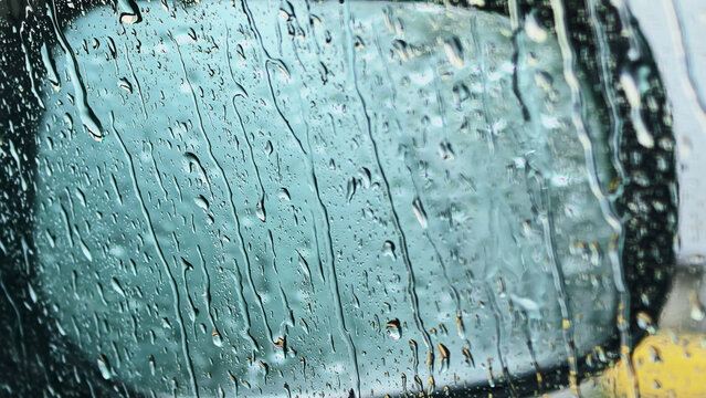 Heavy rain streaks flowing down car window with blurred vehicle outside