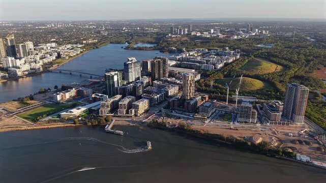 Aerial drone video over Wentworth Point in Sydney, revealing Rhodes in the background, with waterfront apartments, Parramatta River views, urban parkland, and modern residential development in Austral