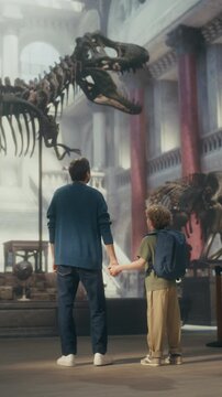Vertical Screen: Natural History Museum With a Father and Young Son Holding Hands, Watching and Learning About a Giant T-rex Dinosaur Skeleton. Family Vacation Fun and Education