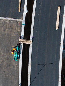Aerial view of road construction workers in orange safety vests operating machinery near a trench on a new road project in Riga, Latvia.