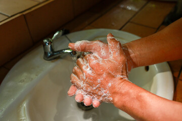Fototapeta premium Washing hands with soap and water in bathroom sink, demonstrating hygiene and cleanliness with foam and bubbles on skin