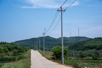 Obraz premium Rural Road with Power Poles and Wind Turbines on Hills