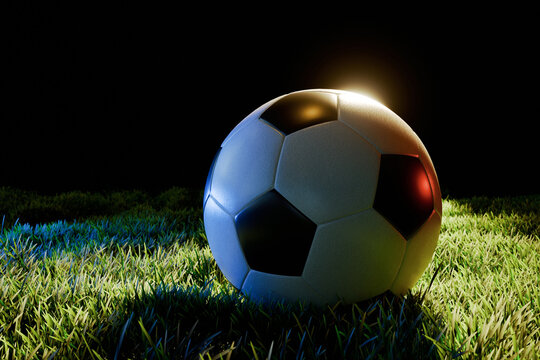 A classic soccer ball resting on green grass at night, dramatically illuminated by vibrant blue and warm golden studio lights against a pitch-black background. Perfect for sports concepts.