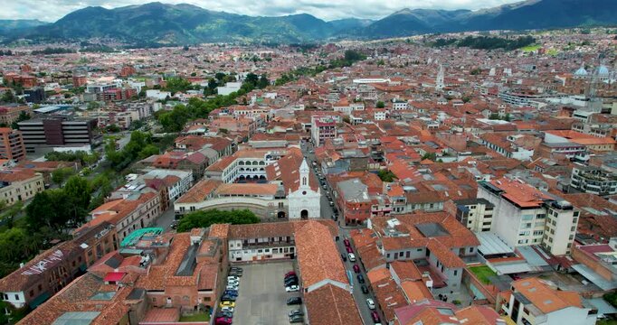 cinematic drone orbit of la merced church in cuenca ecuador showcasing the beautiful tomebamba river with lush green trees on one side and the stunning historic colonial city skyline in the background
