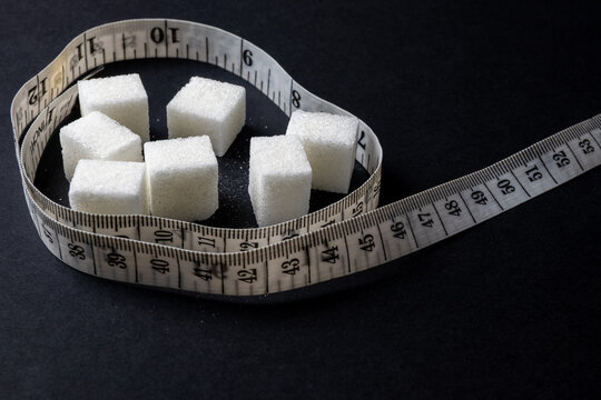 Sugar cubes and measuring tape on black background representing diet concept