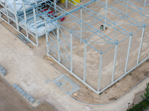 Aerial view of a construction site featuring a steel frame structure and concrete pillars rising from a gravel ground in Riga, Latvia.