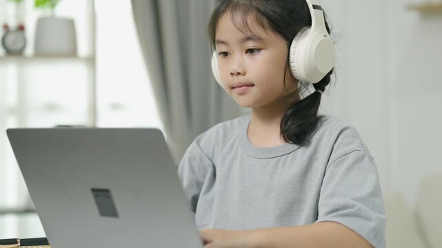 Young girl wearing large headphones and concentrating on laptop in a cozy home setting, creating an educational or entertainment environment
