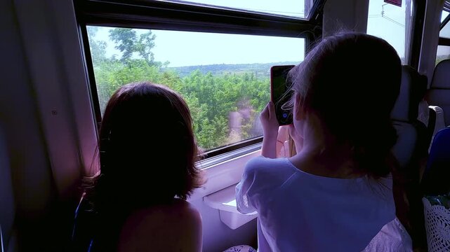 Rear view of a young girl taking photos and video with her smartphone from a train window during a family trip. High quality 4k footage