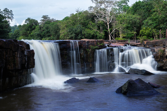 Pristine Tropical Tad Ton Waterfall Cascading Over Dark Rocky Ledges In Chaiyaphum Thailand Surrounded By Lush Green Forest Foliage