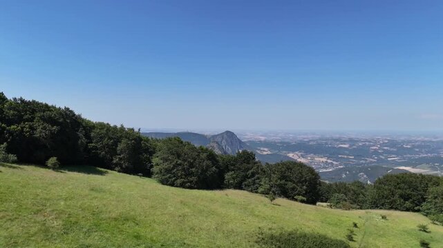 Vista da un drone che sorvola la cima della montagna, scivolando lungo il pendio verso la linea degli alberi e aprendo la vista su un&rsquo;ampia valle con montagne rocciose e paesaggi naturali