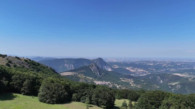 Vista da un drone che sorvola la cima della montagna, scivolando lungo il pendio verso la linea degli alberi e aprendo la vista su un&rsquo;ampia valle con montagne rocciose e paesaggi naturali