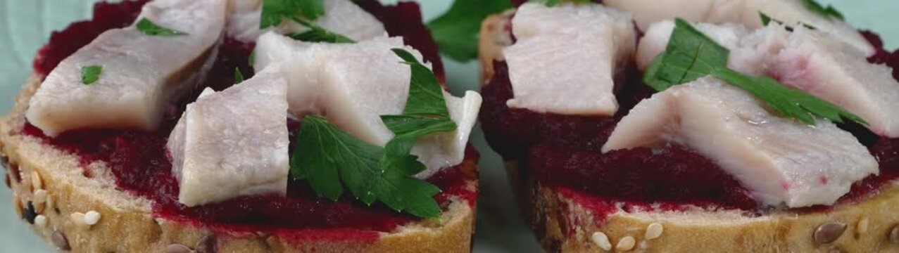 Herring fillets on a whole grain bread with a beet spread and fresh parsley creating a savory healthy meal.