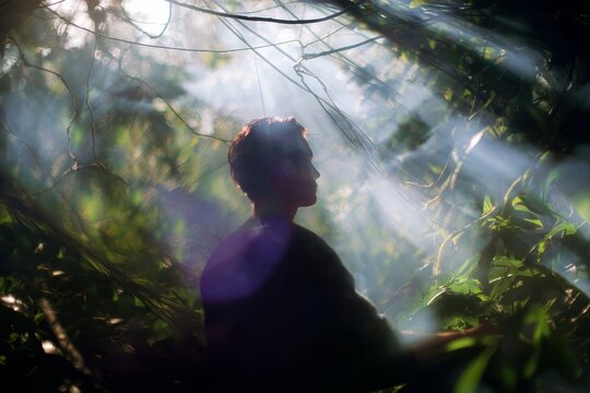 Silhouette person meditating under jungle canopy with sunlight rays through ayahuasca vines for meditation background and spiritual retreat design