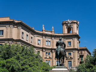 Fototapeta premium Monument to Vittorio Emanuele II at Piazza Giulio Cesare in Palermo, Sicily. Back view of the bronze equestrian statue framing the historic Via Roma entrance buildings under a blue sky.