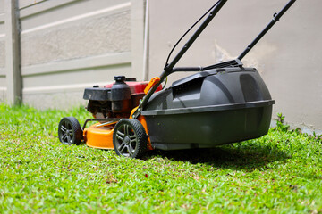 An orange engine-powered lawn mower being used to cut green grass in a backyard garden.