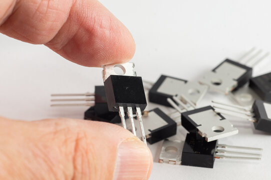 Transistor MOSFET in hand against the background of semiconductors.
