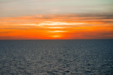 Fototapeta premium Glowing sunset with clouds over the sea. Evening sky in shades of orange. 