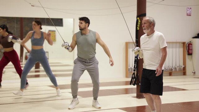 Elderly male fencer practices footwork and blade movements in sports hall