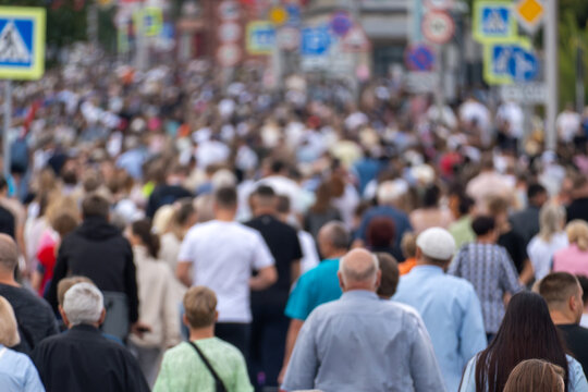 Large crowd of pedestrians walking along a busy city street. Defocused urban scene illustrating population density, everyday commuting, public life and anonymous people.