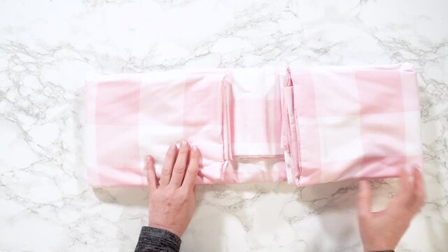 Hands unfolding pink plaid bedding on marble