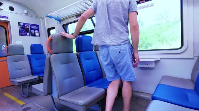 Side view of a mid adult man sitting by the window inside a passenger train car during a summer travel journey. High quality 4k footage