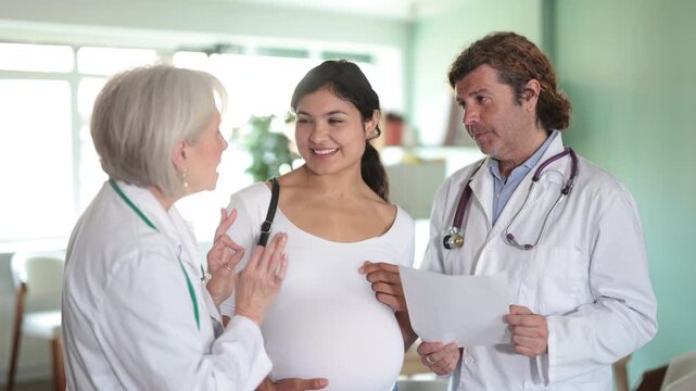 Smiling pregnant woman patient stands with two physicians, elderly woman and adult man, reviewing positive prenatal test results together