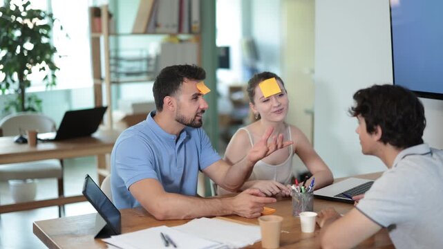 Men and girl with yellow pieces of paper on their foreheads are playing guessing game who am I. Competition for logic, intuition and fun.
