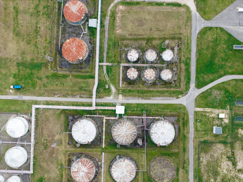 Aerial view of industrial oil storage tanks with rusted and white circular containers connected by pipes in a grassy field in Olaine parish, Olaine Municipality, Latvia.