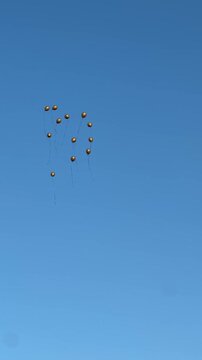 Group of helium balloons with strings flying high in the clear blue sky