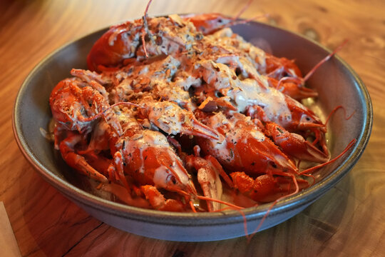 Boiled crayfish served in a bowl with creamy garlic sauce and herbs on a rustic wooden table. Gourmet seafood appetizer, restaurant cuisine, close-up food photography with appetizing presentation.